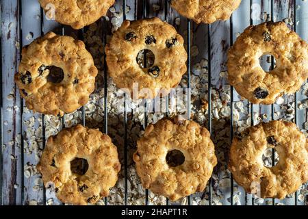 Biscotti di farina d'avena con uvetta e miele fatti su una rastrelliera metallica e alcuni fiocchi d'avena caduti sul tavolo di legno usurato. Concetto di mangiare naturale e sano Foto Stock