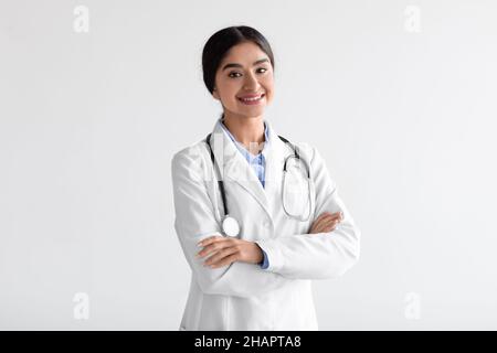 Felice amichevole attraente giovane medico indiano donna in cappotto bianco con stetoscopio con braccia incrociate sul petto Foto Stock