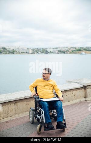 un uomo con disabilità in una sedia a rotelle che cammina guarda il panorama Foto Stock