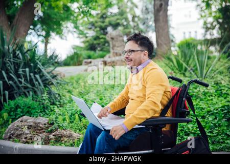 Un uomo con disabilità in sedia a rotelle lavora su un computer su Internet Foto Stock