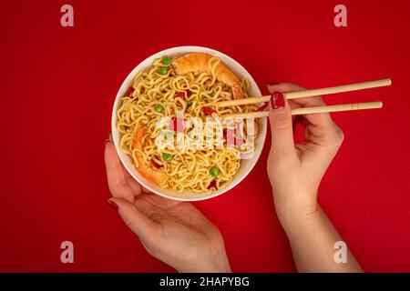 Mani femminili con ciotola di spaghetti di gamberi su sfondo rosso Foto Stock