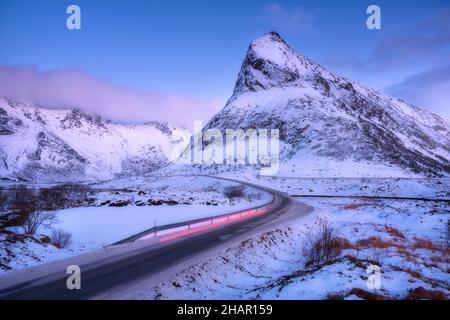 Montagne innevate e fari auto sfocati sulla strada in inverno Foto Stock