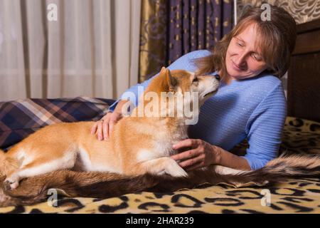 Concetto di amante degli animali domestici. Una donna che si diverte con un cane Shiba Inu su un letto in una camera da letto. Foto Stock