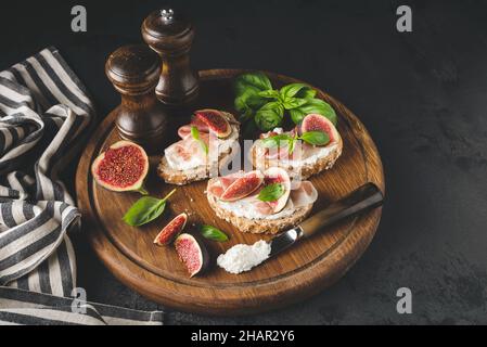 Toast alla bruschetta italiana con prosciutto, ricotta e fichi su tavola di legno. Antipasto sano Foto Stock