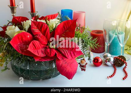 Tavolo da pranzo di natale o di Capodanno con ornamenti speciali, fiore poinsettia, bottiglia di champagne e candele Foto Stock
