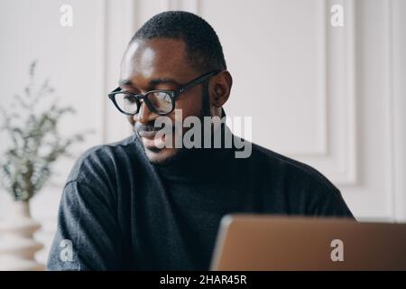 L'uomo Afro-americano pensivo si siede alla scrivania a casa, guarda la video classe online o il webinar sul computer Foto Stock