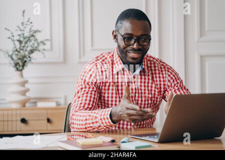 Tutor insegnante online uomo africano positivo guardando lo schermo del laptop e parlando con gli studenti Foto Stock