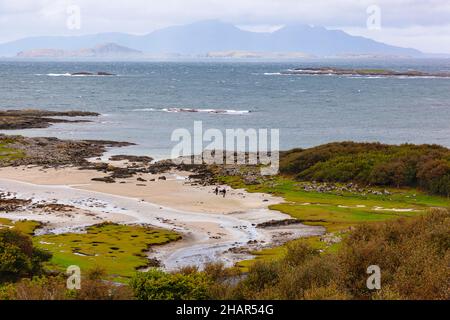 Passeggiate sulla spiaggia di sabbia bianca a Portuairk, l'insediamento più occidentale della terraferma britannica nella Scozia occidentale, con vista sulle piccole isole Foto Stock