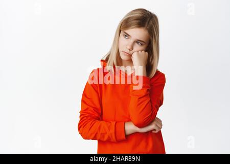 Ritratto di ragazza bionda triste e annoiato, bambino che guarda cupo e sconvolto, in piedi con cappuccio rosso su sfondo bianco Foto Stock