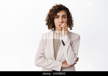 Ritratto di donna d'affari che si sente ansioso, mordere le dita e guardare nervoso, paura di smth, in piedi preoccupato su sfondo bianco Foto Stock