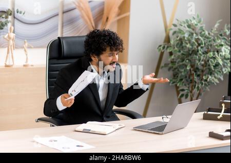 Emotivo arrabbiato infastidito CEO, manager, dipendente indiano o arabo, infastidito a parlare con un collega tramite collegamento video, giuramento per prestazioni scadenti, espressione facciale dispiaciuta, gesti delle mani Foto Stock