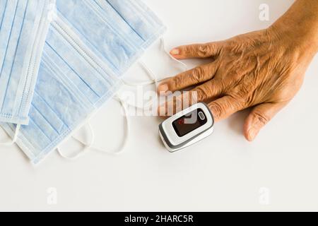 La vecchia mano sta usando di digitale, il bambino infrarosso il termometro allarme di febbre del dito pulsatore ossimetro ossigeno del sangue il monitor di frequenza cardiaca di oximetro vicino le maschere del viso. Foto Stock