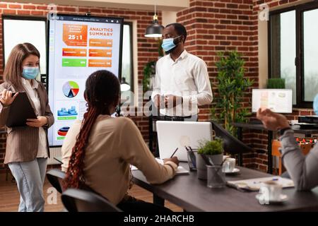 Leader aziendali che mostrano la presentazione di marketing lavorando alla strategia aziendale con businesssteam in startup Office. Gruppo vario di persone che indossa maschera medica per prevenire l'infezione con covid19 Foto Stock