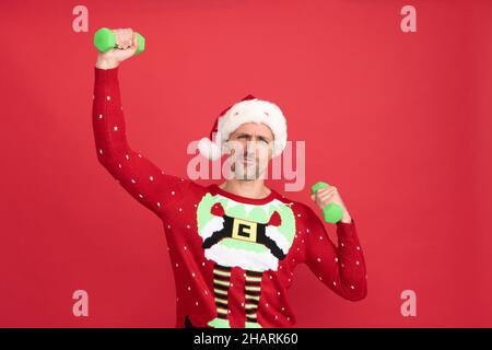 Mai troppo tardi per essere forte. Santa man fare esercizio dumbbell. Bracci flessibili Elf natalizi con pesi a mano Foto Stock