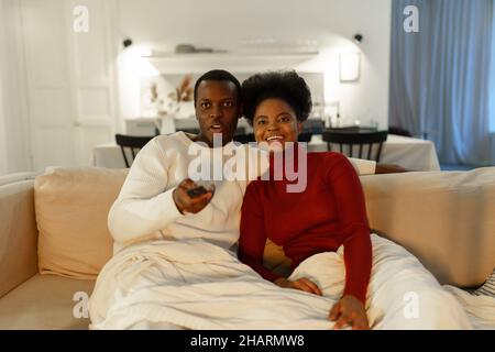 Giovane coppia africana rilassante divano sotto coperta a casa, uomo e donna biraciale guardare la tv insieme Foto Stock