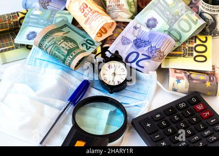 Euro, dollaro USA e banconote turche tagliate su bianco con sveglia vintage, calcolatrice, penna, lente d'ingrandimento e maschere mediche. Immagine concettuale Foto Stock