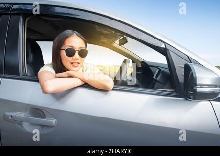 Donna asiatica con occhiali da sole appoggiati sulla vetrinetta Foto Stock