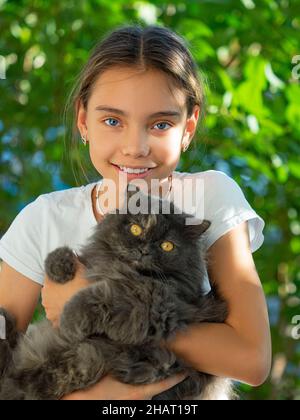 Una ragazza che tiene in mano un gatto nero parassita tra le braccia sorride e guarda la fotocamera. Concetto di cura degli animali. Foto Stock