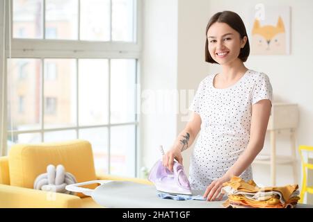 Giovane donna incinta che stira calzini a casa Foto Stock