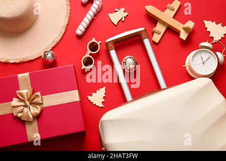 Composizione con valigia, sveglia, accessori femminili e decorazioni su sfondo rosso, primo piano. Vacanza di Natale concetto Foto Stock