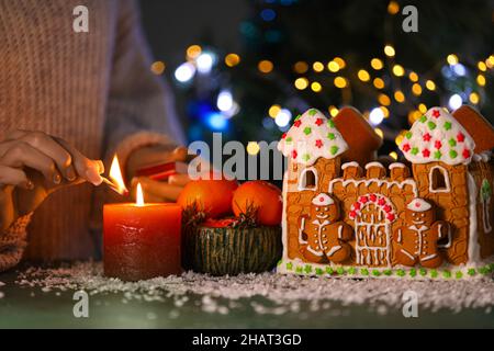 Casa di pan di zenzero e donna che illuminano la candela al tavolo contro sfondo sfocato, primo piano Foto Stock