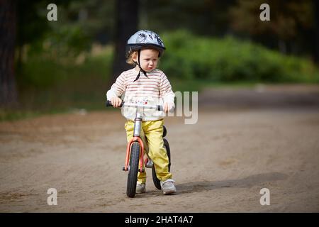 ragazza in un casco corre su una bicicletta balance in una giornata estiva soleggiata Foto Stock