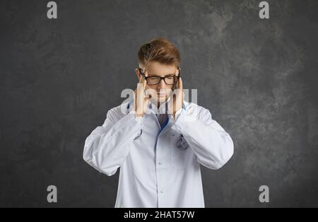 Ritratto di giovane medico esausto di sesso maschile che avverte grave mal di testa e malessere. Foto Stock