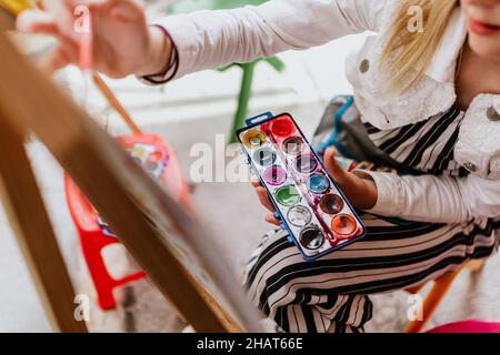 Mano di teen girl artista con tavolozza e pennello pittura acquerello su carta in terrazza in america latina Foto Stock