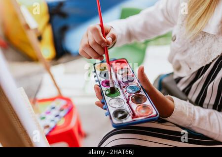 Mano di teen girl artista con tavolozza e pennello pittura acquerello su carta in terrazza in america latina Foto Stock