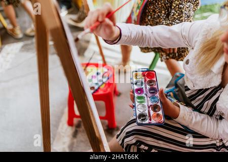 Mano di teen girl artista con tavolozza e pennello pittura acquerello su carta in terrazza in america latina Foto Stock