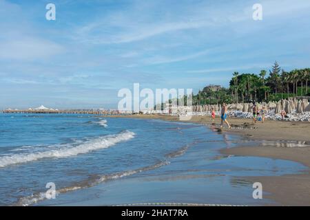 Vista sulla spiaggia, lettini, ombrelloni, bandiere e piccola costa ondulata sul lato di Antalya. Messa a fuoco selettiva. Foto Stock