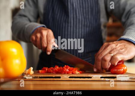 Primo piano di mani, anziani multiculturali maschi tritare verdure per la colazione. Pensionato, sano a casa. Foto Stock