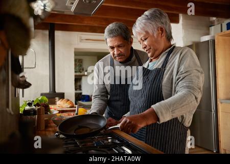 Felice multi-culturale anziani coppia illuminazione stufa a gas per cucinare insieme sana colazione in cucina moderna. Foto Stock