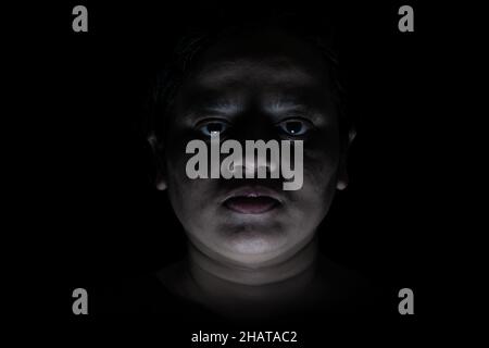 Il volto femminile di Spooky si nasconde in ombra con un'espressione seria e creepy, isolato su sfondo nero Foto Stock
