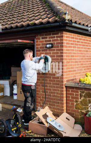 Elettricista che monta un caricabatterie per auto elettrica Zappi alla parete esterna di un garage privato. NB: I locali nella fotografia sono proprietà liberate. Foto Stock