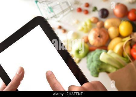 Premere con le dita lo schermo del dispositivo mobile per effettuare l'ordine di acquisto in un supermercato con la borsa della spesa e lo sfondo del carrello. Vista dall'alto. Composizione orizzontale Foto Stock