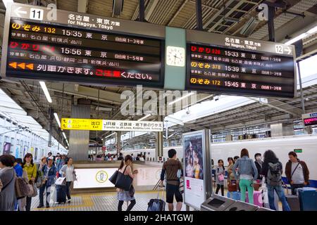 Un gran numero di persone in attesa sul binario alla stazione ferroviaria di Kyoto con un grande treno orari bordo informazioni appeso al soffitto. Foto Stock