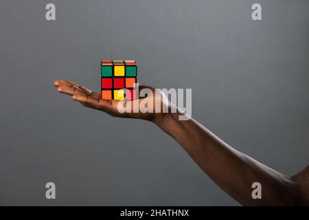 Raccolto irriconoscibile persona afroamericana che dimostra colorato Rubik's cubo su sfondo grigio in studio Foto Stock