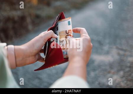 Una donna irriconoscibile prende una banconota da 50 euro da un portafoglio in pelle rossa per strada. Concetto di pagamento, salario e bancario. Foto Stock