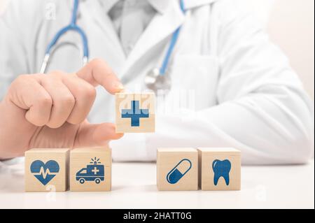 Mano del medico scegliere il segno della croce sul blocco del cubo di legno. Icona medica di sanità sui blocchi di legno. Medico in cappotto bianco che dispone i cubi con i simboli medici Foto Stock