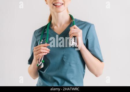 Primo piano scatto ritagliato di irriconoscibile medico sorridente in verde uniforme medica con stetoscopio intorno al collo. Foto Stock