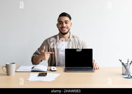 Happy Arab Guy che mostra notebook con schermo nero vuoto, Mockup Foto Stock