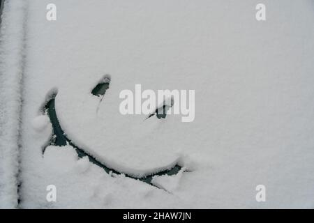 Sfondo di neve. Trama di neve bagnata con un allegro motivo simbolo sorridente nella finestra invernale della vettura all'aperto da vicino. Sorridete nella neve, felice Foto Stock