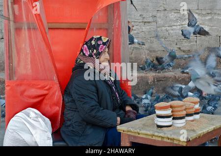 Donna anziana con foulard che vende cibo piccione volante, Istanbul, Turchia Foto Stock