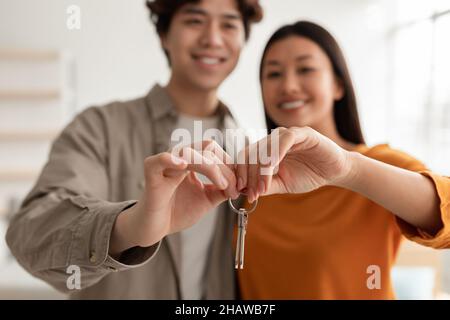 Felice coppia millenaria asiatica che mostra la chiave della casa, passando insieme a un nuovo appartamento, fuoco selettivo Foto Stock