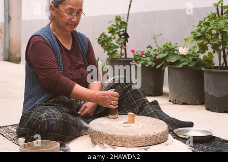 L'antico mulino a mano o pietra di quern, macina il grano in farina. Vecchie pietre di macinazione fatte a mano. La vecchia donna macina la farina con la tradizionale Foto Stock