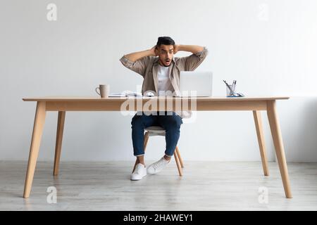 Scioccato ragazzo arabo afferrare la testa utilizzando il portatile Foto Stock