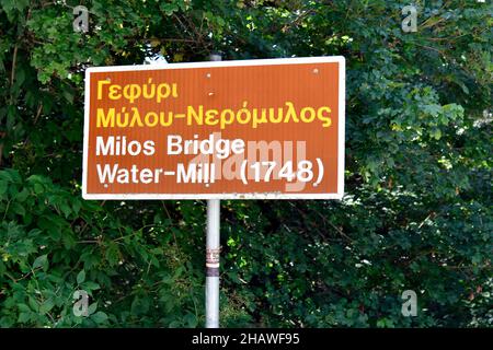 Grecia, Epiro, cartello per il ponte medievale in pietra di Milos e mulino ad acqua in greco e latino script Foto Stock