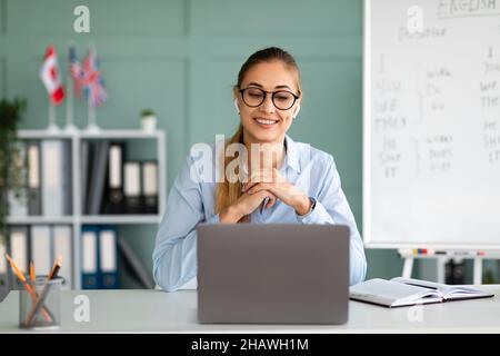 Tutoraggio online delle lingue straniere. Ragazza allegra insegnante di inglese che dà in classe online, comunicando su laptop Foto Stock