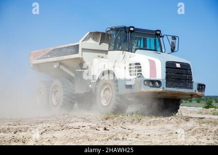 Dumper articolato di grandi dimensioni con cabina bianca in cantiere durante lavori di scavo contro il cielo blu. Carico e trasporto del terreno . DUS Foto Stock